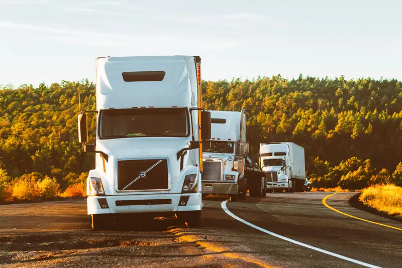 Tres camiones en fila por una carretera al atardecer